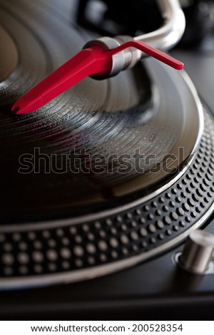 Close up detail view of a record player with a red needle touching the groove of a vinyl album playing music, interior. Still life professional musical equipment objects.