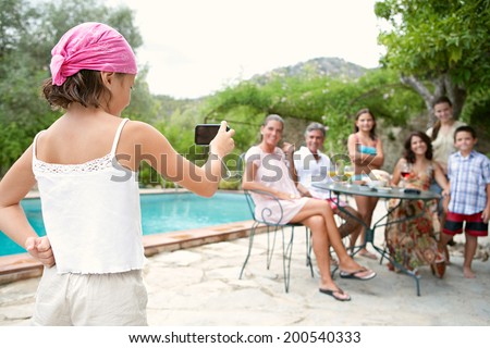 Large family group sitting together around a table with food and drink in a summer holiday hotel garden with swimming pool, posing for a photograph during a vacation together. Active family lifestyle.