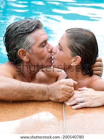 Portrait close up of a mature loving couple relaxing together in a swimming pool in a holiday hotel, enjoying a summer vacation and kissing. Senior couple outdoors lifestyle and romantic activities.
