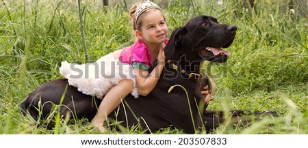 Panoramic view of a pretty young girl wearing a pink fancy dress, sitting on her dogs back enjoying a sunny holiday in a green park field, hugging him outdoors. Active family with pets, lifestyle.