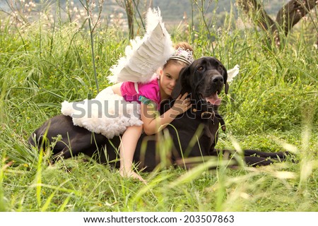 Side view of a young girl wearing a pink fancy dress with wings, sitting on her dogs back enjoying a sunny holiday in a green park field, hugging him outdoors. Active family with pets, lifestyle.