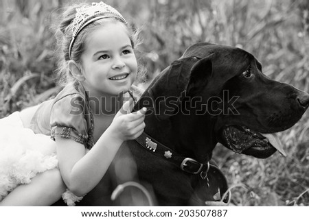 Black and white close up portrait of a beautiful young girl wearing a fancy dress, sitting on her dog pet back, smiling and enjoying a summer holiday. Active family with pets outdoors lifestyle.