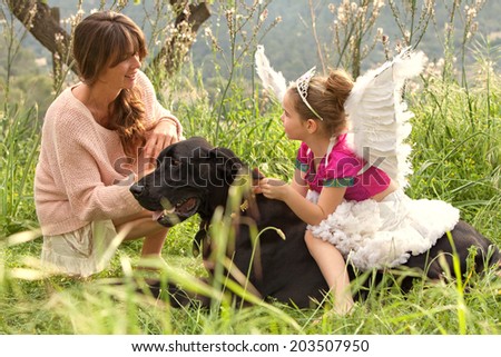 Mother and young daughter relaxing together with their pet dog in a lush green field on holiday during a sunny day. Animal pets, friendship and companionship. Active family caring for their dog.
