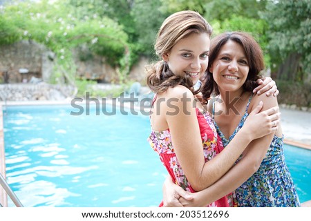 Portrait of an attractive teenager daughter and her mother hugging and smiling during a summer holiday break in a vacation villa green garden and swimming pool, relaxing together. Outdoors lifestyle.
