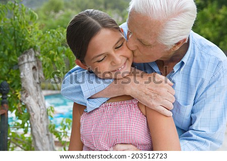 Close up family portrait of a grandfather and his granddaughter hugging and kissing while on a summer vacation in a holiday villa green garden with swimming pool. Loving relatives outdoors lifestyle.