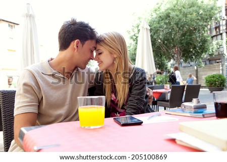Profile portrait of an attractive young couple on holiday being romantic and holding their heads together while sitting at a coffee terrace bar drinking refreshments during a summer vacation outdoors.