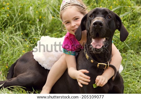 Close up view of a beautiful young girl riding her grate dane pedigree pet dog while dressing up as a princess during a summer day in a green field, outdoors. Animal friendship fun and love lifestyle.