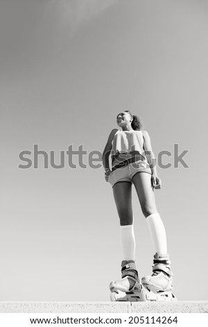 Black and white view of a young teenager girl with colorful clothes, smiling while roller skating against a bright clear sky during a sunny summer holiday break. Sport fun and lifestyle, outdoors.
