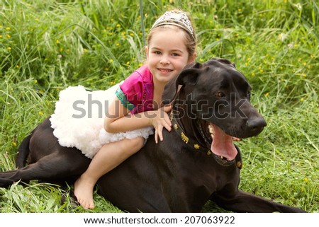 Beautiful girl child and her labrador pet dog hugging while girl sits on the animal back, enjoying a summer holiday in a green grass field wearing a fancy dress. Fun activities and children lifestyle.
