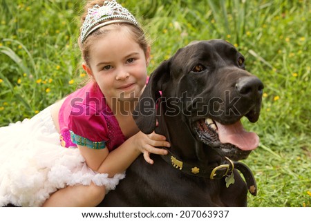 Beautiful girl child and her labrador pet dog hugging while girl sits on the animal back, enjoying a summer holiday in a green grass field wearing a fancy dress. Fun activities and children lifestyle.