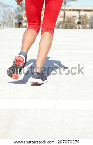 Close up rear view of a young woman legs jogging and doing exercise during a sunny day, wearing red sport wear and running on a flat pavement in a city, outdoors. Healthy sport lifestyle.