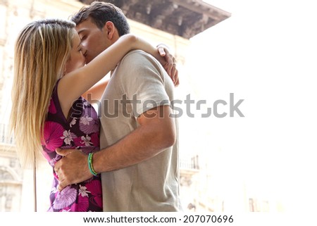 Side view of a romantic young couple kissing each other with passion in a city street during a sunny day on holiday, outdoors. (People, Lifestyle, Romance)