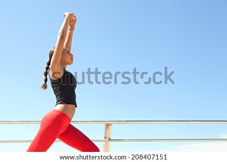 Profile view of an athletic and sporty young african american black woman stretching her legs and body while exercising on a sunny day against a bright blue sky. Sport active lifestyle outdoors.