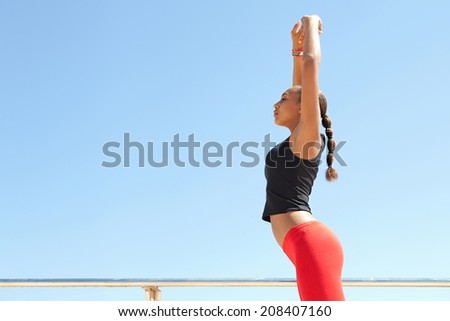 Profile view of an athletic and sporty young african american black woman stretching her legs and body while exercising on a sunny day against a bright blue sky. Sport active lifestyle outdoors.