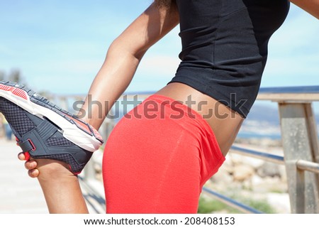 Close up side view of a healthy woman middle body section stretching her legs while exercising by the seaside, holding and pulling her muscles during a sport training day. Sporty lifestyle outdoors.