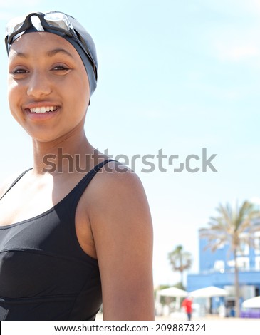 Portrait of a healthy sporty african american young woman swimmer standing on a sunny beach wearing goggles and a swimming cap, exercising and training outdoors. Sport lifestyle outdoors.