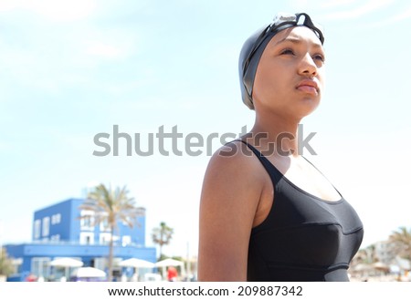 Portrait of a healthy sporty african american young woman swimmer standing on a beach with goggles and a swimming cap, training outdoors feeling strong and confident. Sport lifestyle outdoors.
