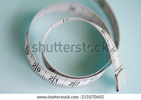 Close up still life detail view of a soft tailor measuring tape laying in a curly circle shape on a plain blue background, interior. Trade tools and objects for exact measure taking.