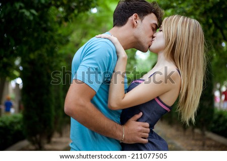 Side view of a passionate romantic young couple kissing and embracing while in a green park on holiday. Young people romantic lifestyle and love, outdoors.