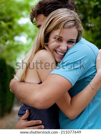 Side portrait view of a young tourist couple in love, embracing with joyful expressions while visiting a romantic green park on holiday, traveling. Lovers outdoors lifestyle.