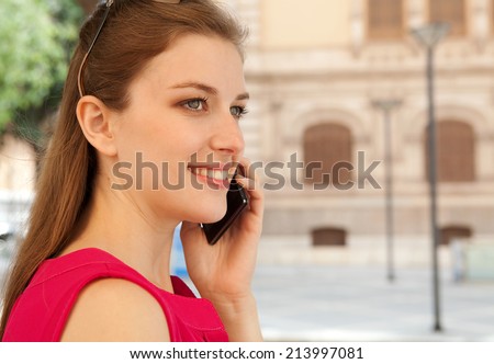 Close up profile portrait of a beautiful young business woman using a smartphone in the city to make a call and have a conversation, smiling in a classic street. Professional woman using technology.