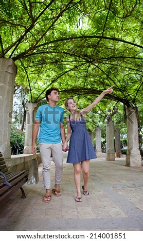 Attractive young tourist couple visiting a green garden park on a weekend city travel break, pointing at monumental sights. Loving girlfriend and boyfriend enjoying a summer holiday outdoors.