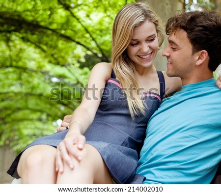 Attractive young tourist couple sitting down on a  wooden bench while visiting a green garden park on a weekend city travel break. Loving girlfriend and boyfriend enjoying a summer day outdoors.