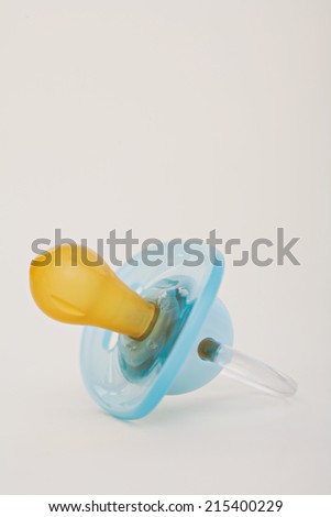 Still life close up view of a new born baby boy blue dummy laying isolated on a plain white background, indoors. Detail of plastic and rubber baby dummy.