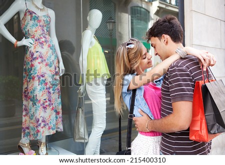 Portrait of a attractive young couple having fun together and enjoying a vacation city break, embracing and smiling while shopping in the fashion stores, outdoors. Consumer and travel lifestyle.