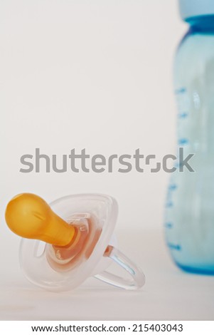 Close up still life of a baby dummy and feeding bottle together on a white background. Detail view of a nursery new born items.