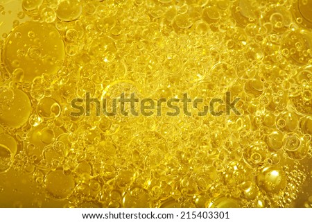 Over head close up full frame background detail view of golden shining yellow oil boiling and creating bubbles, indoors. Macro still life view of oil bubbles texture and detail.
