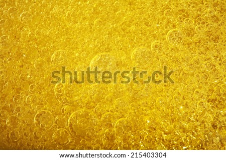 Over head close up full frame background detail view of abstract golden shining yellow oil boiling and creating bubbles, indoors. Macro still life view of oil bubbles texture and detail.