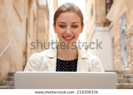 Portrait of an attractive young professional business woman sitting on the steps of an old stone building street using a laptop computer working outdoors. Connectivity and wireless internet browsing.
