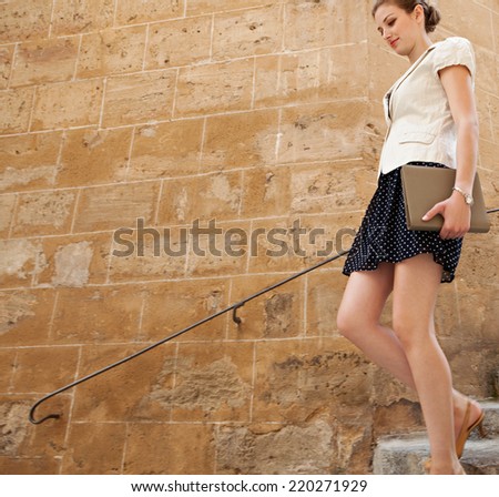 Side view of businesswoman walking down the steps of a stone buildings street in a classic city, holding a folder with paperwork and feeling positive outdoors. Business people.