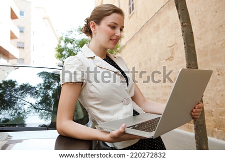 Portrait of elegant business woman in a classic city with textured stone buildings and walls, holding a high technology smartphone in her hand, smiling at the camera outdoors. People and technology.