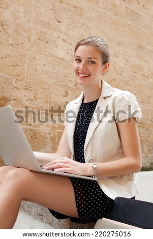 Attractive young professional business woman sitting on the steps of an old stone building using a laptop computer working outdoors. Connectivity and wireless internet browsing.