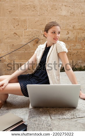 Serene and attractive young professional business woman sitting on the steps of an old stone building using a laptop computer working outdoors. Connectivity and wireless internet browsing.