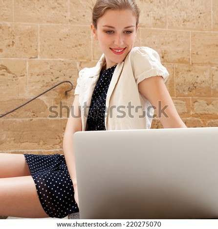 Attractive young professional business woman sitting on the steps of an old stone building using a laptop computer working outdoors. Connectivity and wireless internet browsing.