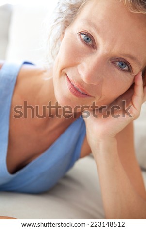 Close up beauty portrait of an attractive middle aged healthy woman blue eyes, relaxing at home and looking at the camera smiling. Interior home living and well being lifestyle.