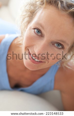 Close up beauty portrait of an attractive middle aged healthy woman relaxing on a white sofa at home, looking at the camera smiling. Interior home living and well being lifestyle.