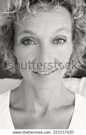 Black and white portrait of a healthy and attractive blond woman with blue eyes, smiling and looking at the camera while relaxing on a white sofa at home, interior. Home living and healthy lifestyle.
