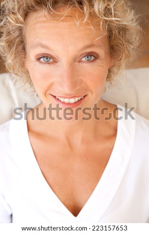 Close up beauty portrait of a healthy and attractive blond woman with blue eyes, smiling and looking at the camera while relaxing on a white sofa at home, interior. Home living and healthy lifestyle.