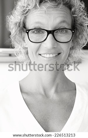 Black and white close up portrait of a joyful professional successful woman smiling at the camera feeling confident in an office interior. Businesswoman wearing reading glasses indoors.