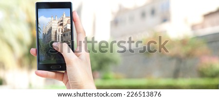 Panoramic view of a young woman hand holding a smart digital phone device taking pictures of characterful architecture cathedral, visiting a destination city on holiday. Vacation technology lifestyle.