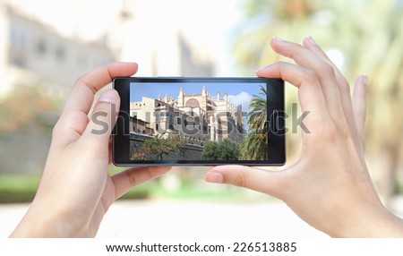 Close up of a young woman hands holding a smart digital phone device taking pictures of a characterful architecture cathedral, visiting a destination city on holiday. Vacation technology lifestyle.