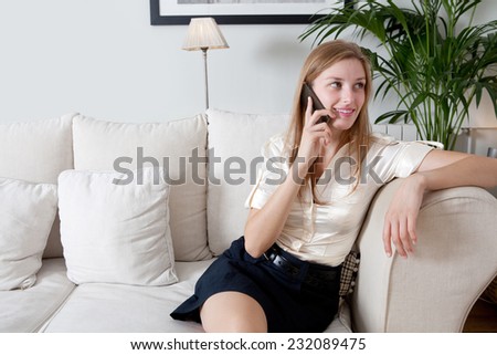 Attractive professional businesswoman sitting on a coach at home living room, working on a laptop computer and making a phone call with a smartphone, indoors. Working from home office.