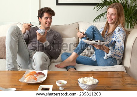 Attractive young couple having a night in at home and enjoying eating japanese take away food in each other\'s company. Couple relaxing on home sofa eating exotic food in a stylish home interior.