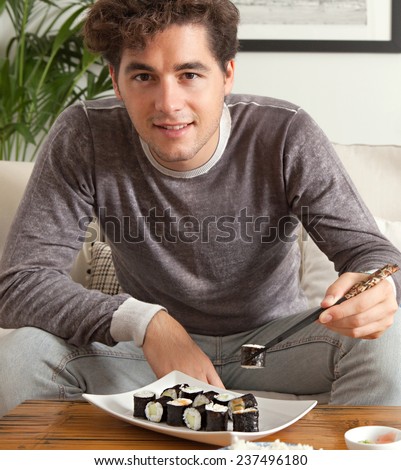 Portrait of attractive young man enjoying eating japanese take away food in living room. Professional man relaxing on home sofa eating exotic food in a stylish home interior.