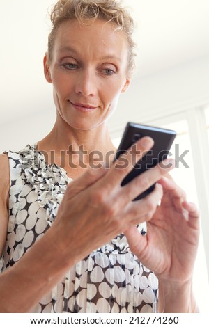 Portrait of an attractive mature professional business woman standing in an office space and using a smartphone device to connect on line, workplace interior. Senior businesswoman using technology.