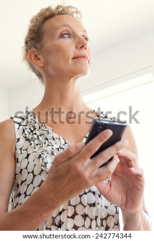 Portrait of a thoughtful powerful mature professional business woman in an office space, using a smartphone device to connect on line, workplace interior. Senior businesswoman using technology.